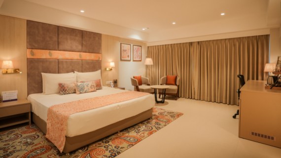 Premium room with king-sized bed, lounge chairs and floor-length curtains at Maharashtra Bhuvan